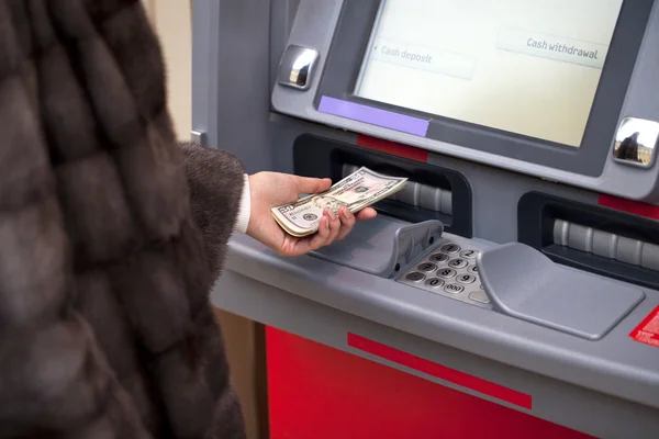 Женщина показывает банкноты в долларах перед банкоматом — стоковое фото