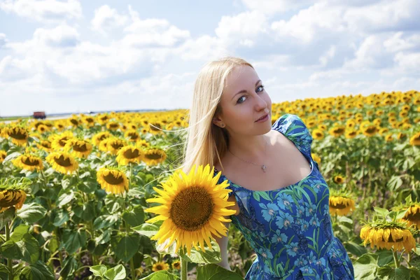 Portret van een mooie jonge blonde vrouw in blauwe jurk op een ba — Stockfoto