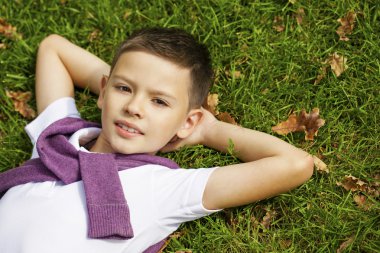 Brunette little boy laying on the grass in the park clipart