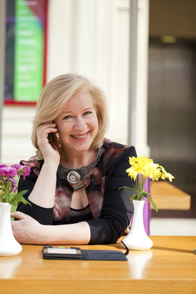 Mature beautiful woman is calling on a cell phone while sitting — Stock Photo, Image