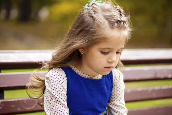 Sad little girl is sitting on the bench, outdoor shoot — Stock Photo, Image