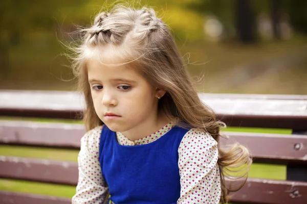 Sad little girl is sitting on the bench, outdoor shoot — Stock Photo, Image