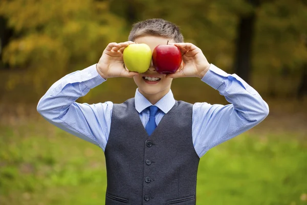 Malý chlapec drží červené a zelené jablko na pozadí autu — Stock fotografie