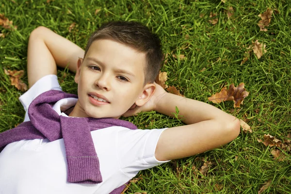 Brunette little boy laying on the grass in the park — Stock Photo, Image