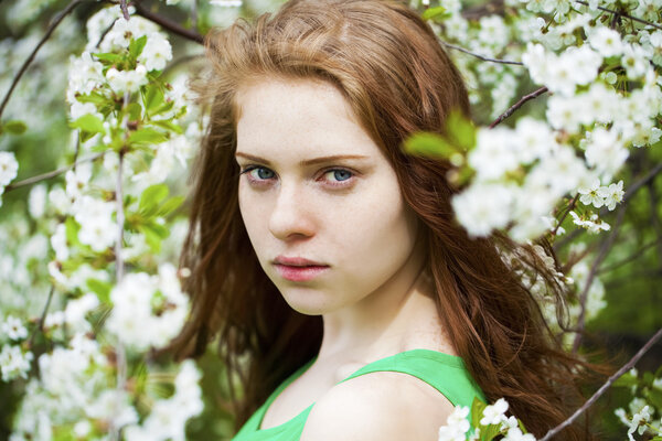 Beautiful young girl standing near blooming trees in spring gard