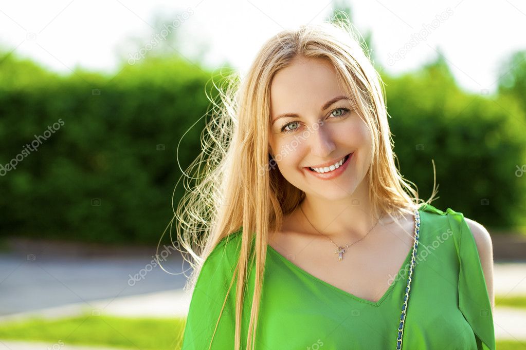 Young beautiful woman in green dress posing outdoors in sunny we