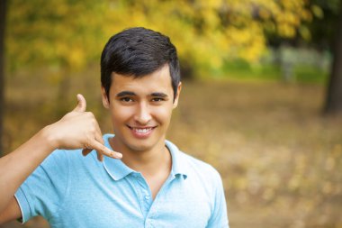 Attractive man making a call me gesture, outdoors autumn park clipart