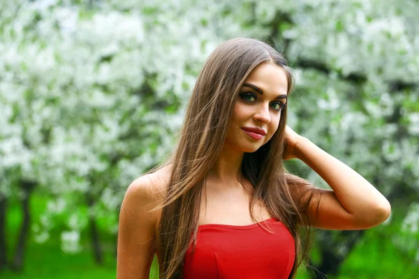 Happy young woman in red dress against the background spring flo — Stock Photo, Image