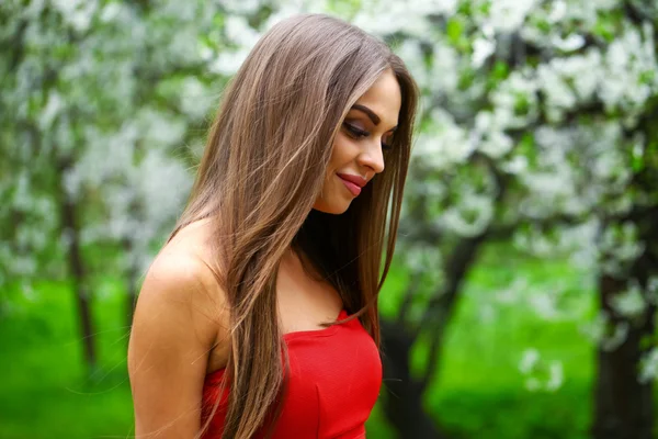 Happy young woman in red dress against the background spring flo — Stock Photo, Image