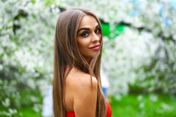 Happy young woman in red dress against the background spring flo — Stock Photo, Image