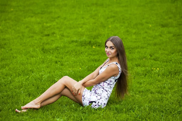 Mulher sexy em vestido curto sentado na grama verde — Fotografia de Stock