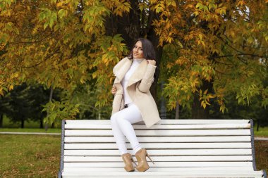 Sonbaharda bir bankta oturan güzel genç esmer kadın 