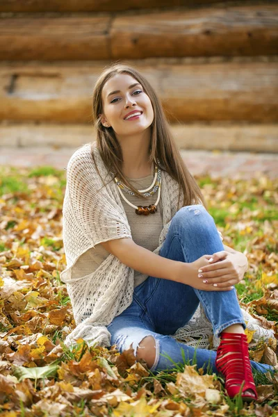 Feliz hermosa mujer en pantalones vaqueros azules sentado en el parque de otoño —  Fotos de Stock