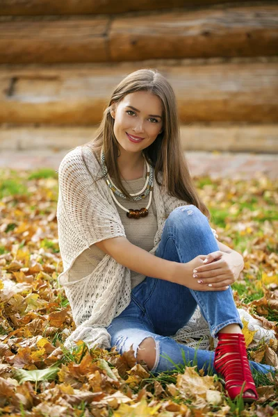 快乐美丽的女人，穿着蓝色牛仔裤坐在秋天的公园 — 图库照片