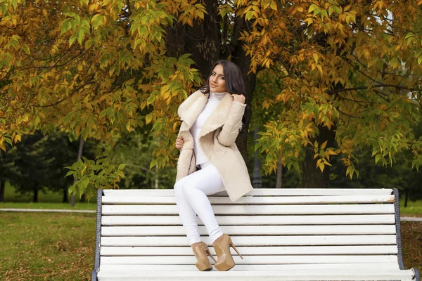 Mooie jonge brunette vrouw zittend op een bankje in de herfst — Stockfoto