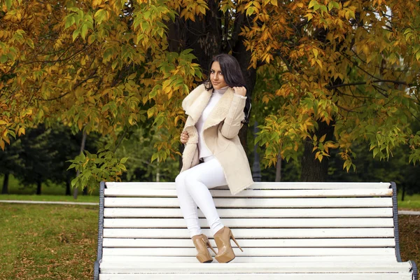 Beautiful young brunette woman sitting on a bench in the autumn — Stock Photo, Image