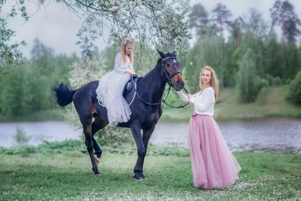 Flicka på svart häst i blossom trädgård — Stockfoto