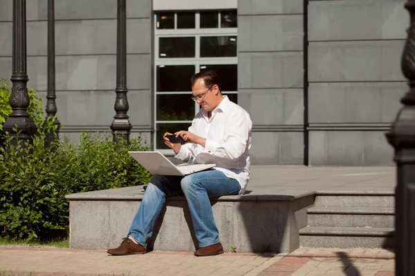 Дорослий чоловік з комп'ютером сидить на відкритому повітрі сонячний день — стокове фото