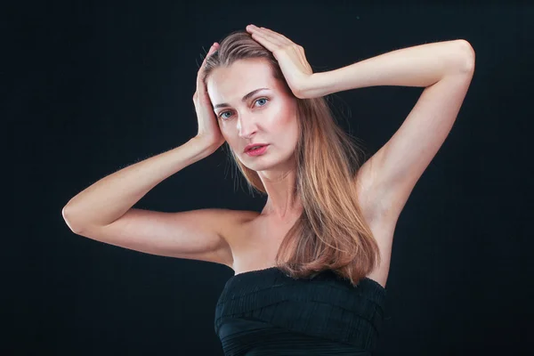 Mujer bonita sosteniendo la cabeza en las manos de pie contra backgr negro — Foto de Stock