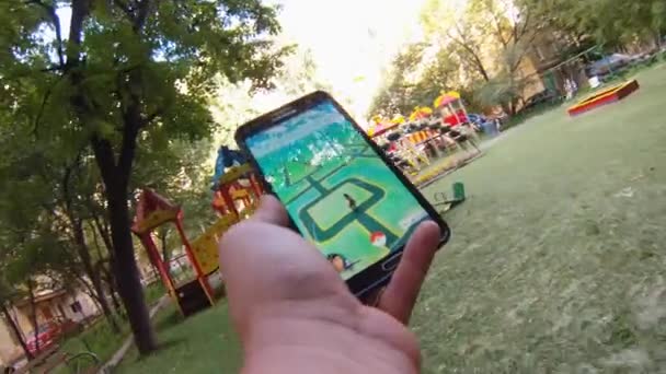 Pokemon Go aplicativo sendo jogado por um homem em seu telefone celular enquanto caminhava no jardim . — Vídeo de Stock