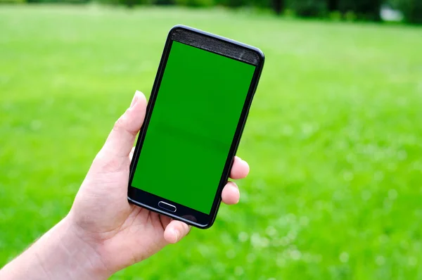 Ember szúró telefon tartja kezében, zöld tavaszi háttér — Stock Fotó