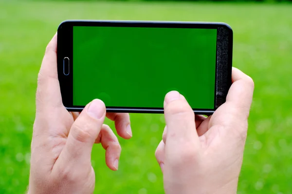 Ember szúró telefon tartja kezében, zöld tavaszi háttér — Stock Fotó