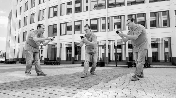 Drei Männer mit Mobiltelefon vor einem weißen Geschäftszentrum — Stockfoto