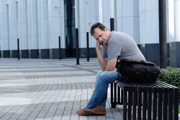 Homem triste sentado na frente do prédio de escritórios branco — Fotografia de Stock