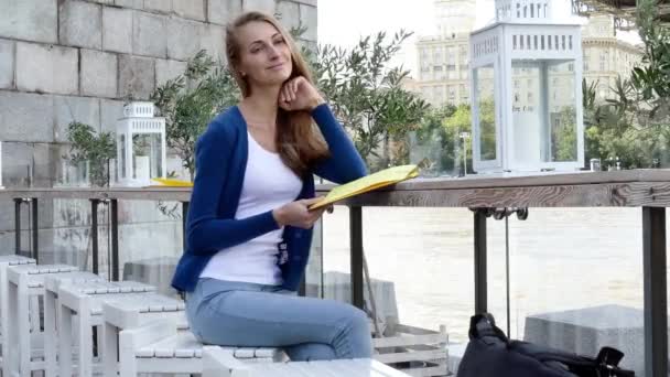 Νεαρή γυναίκα ευτυχισμένη ανάγνωση μενού στην καφετέρια του δρόμου ημέρα του φθινοπώρου — Αρχείο Βίντεο
