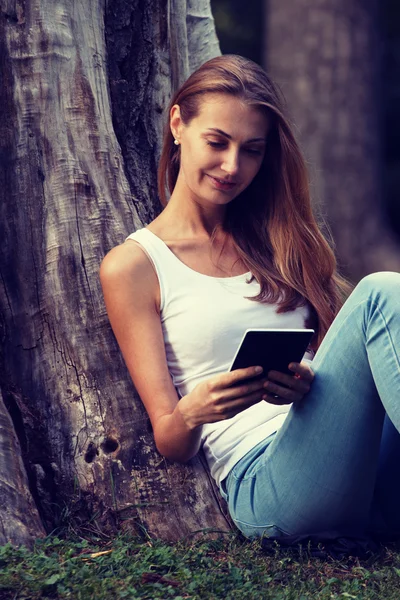 Молодая женщина сидит на траве и читает электронную книгу на открытом воздухе. Вин — стоковое фото