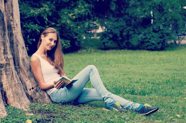 Jeune femme assise sur l'herbe et le livre de lecture en plein air . — Photo