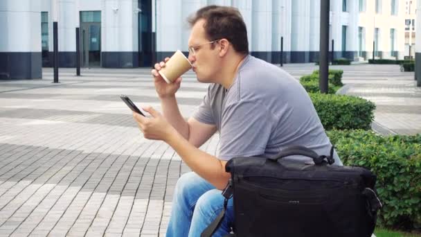 Ao estilo da cidade. Bonito homem adulto em desgaste casual usando café do telefone móvel na frente do prédio de negócios branco . — Vídeo de Stock