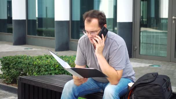 Stijl van de stad. Knappe volwassen man in vrijetijdskleding met behulp van de mobiele telefoon koffie voor witte zakelijke gebouw. — Stockvideo