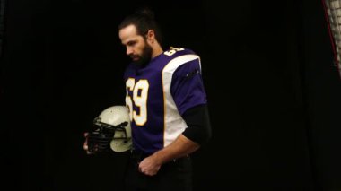 Siyah arka planda Amerikan Futbolcusu yavaşça kameraya doğru dönüyor.