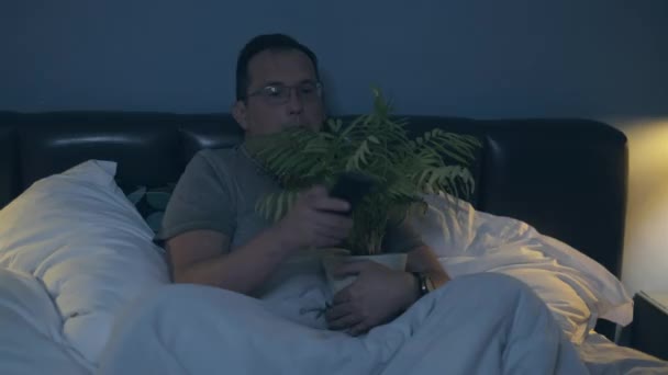 Чоловік дивиться фільм жахів обіймається з домашньою квіткою — стокове відео