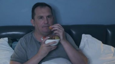 Televizyon izleyen ve meyve yiyen bir adam.