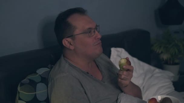 Чоловік дивиться телевізор і їсть фрукти — стокове відео