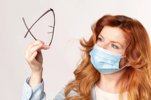 Woman examines her glasses that fog up when wearing a medical mask — Stock Photo, Image