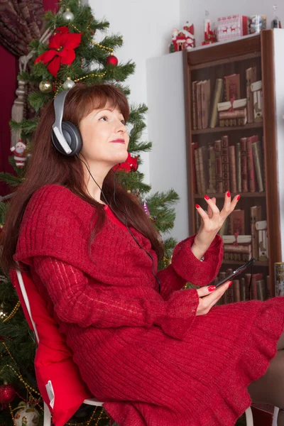 Mulher adulta ouvindo música contra a árvore de Natal — Fotografia de Stock