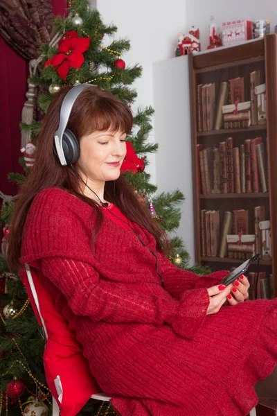 Volwassen vrouw luisteren muziek tegen kerstboom — Stockfoto