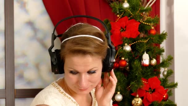 Hermosa mujer adulta escuchando música contra el árbol de Navidad — Vídeos de Stock