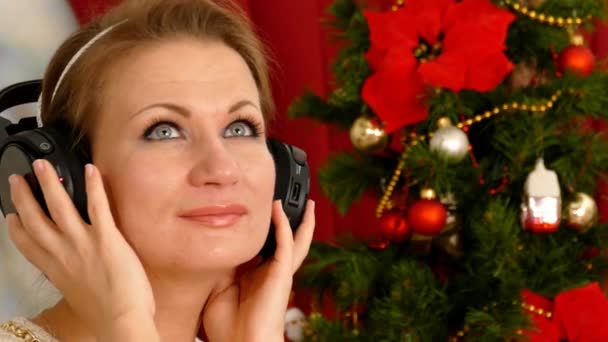 Mulher adulta bonita ouvindo música contra a árvore de Natal — Vídeo de Stock