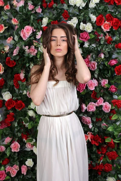 年轻漂亮的女人在花墙上的白色连衣裙 — 图库照片