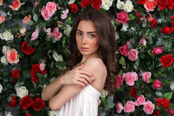 Jolie jeune femme en robe blanche sur le mur de fleurs — Photo