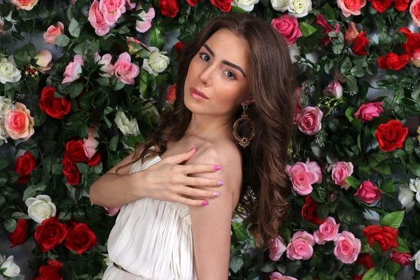 Приваблива молода жінка в стильній білій сукні на квітковій стіні — стокове фото