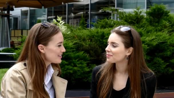 Две девушки пьют кофе на скамейке перед бизнес-центром — стоковое видео