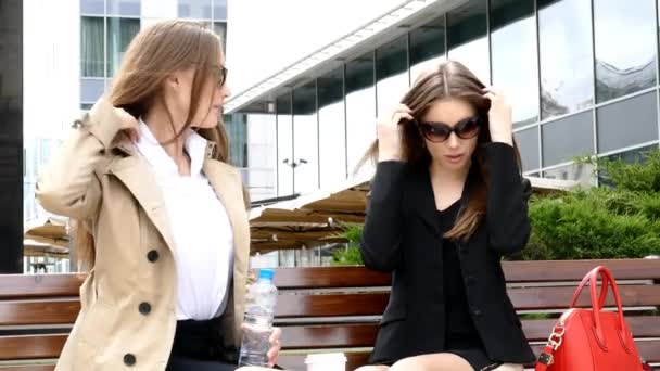 Dos chicas tomando café en el banco frente al centro de negocios — Vídeos de Stock