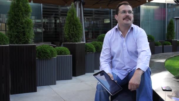 Adult man wearing headphone using tablet computer on the stairs. — Stock Video