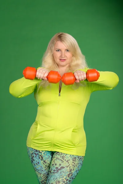 Mujer de talla grande bombeando músculos con mancuernas en la espalda verde —  Fotos de Stock