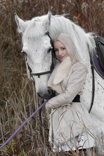 Blondýnka s bílým koněm na západu slunce stojí dohromady — Stock fotografie